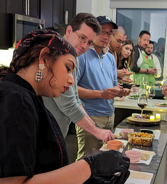Participants in cooking class in Queens, NY watching as instructor teaches them how to prepare dish